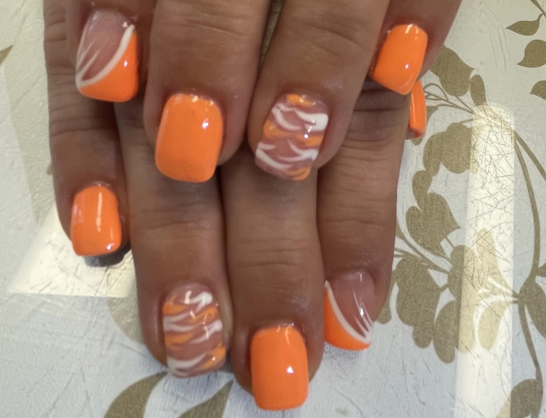 Closeup image of a woman's nails, showing various designs of solid orange and orange and white .